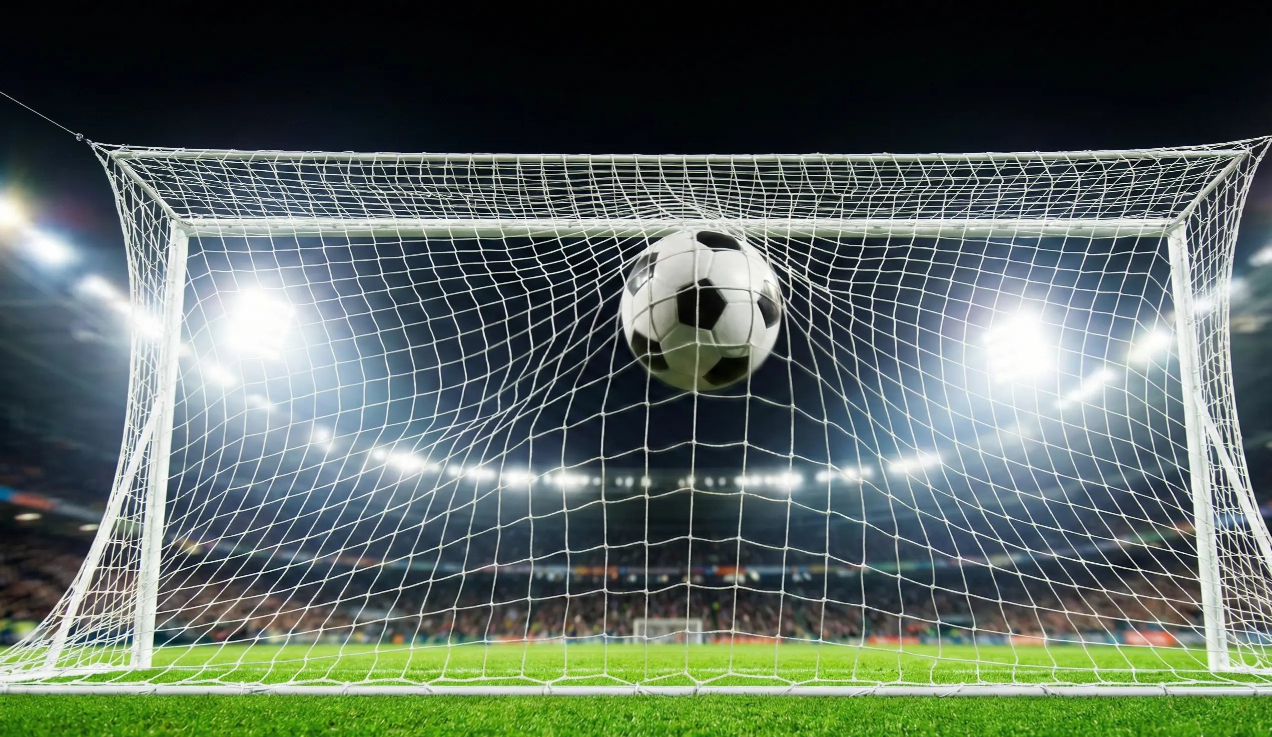 Football flying into the goal net during a Champions League match at night